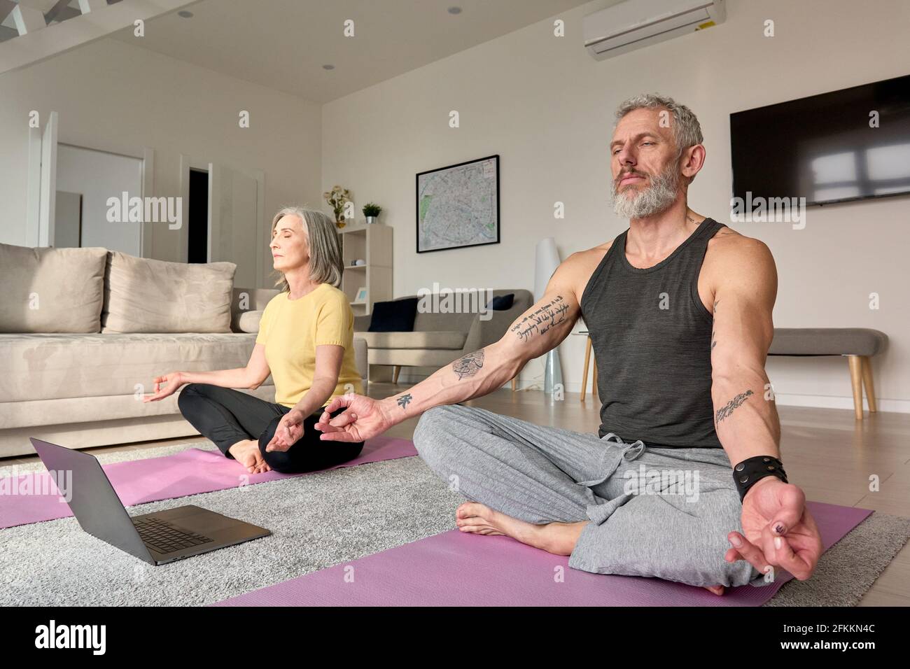La coppia anziana meditating facendo yoga virtuale pone guardare la classe in linea a casa. Foto Stock
