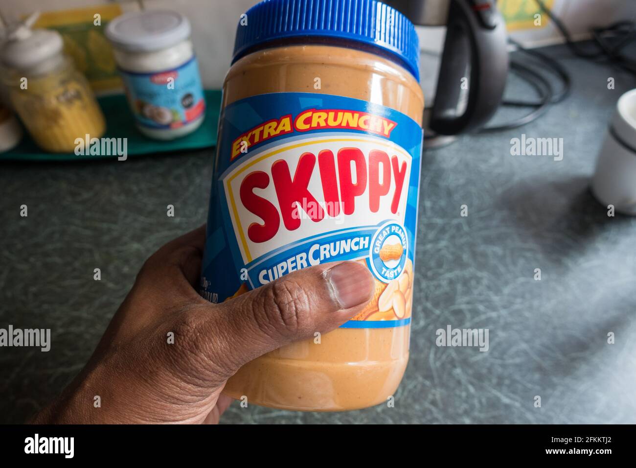 Barattolo di burro di arachidi Skippy tenuto da un maschio adulto con gli articoli della cucina sullo sfondo Foto Stock