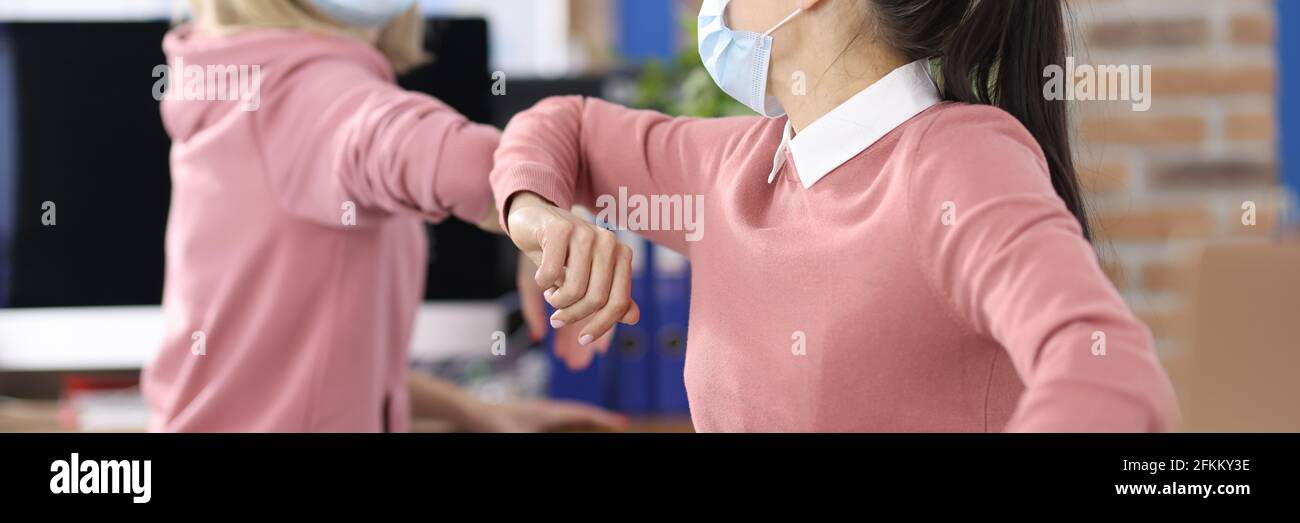 Due donne in ufficio in maschere mediche protettive salutano in modo sicuro Foto Stock