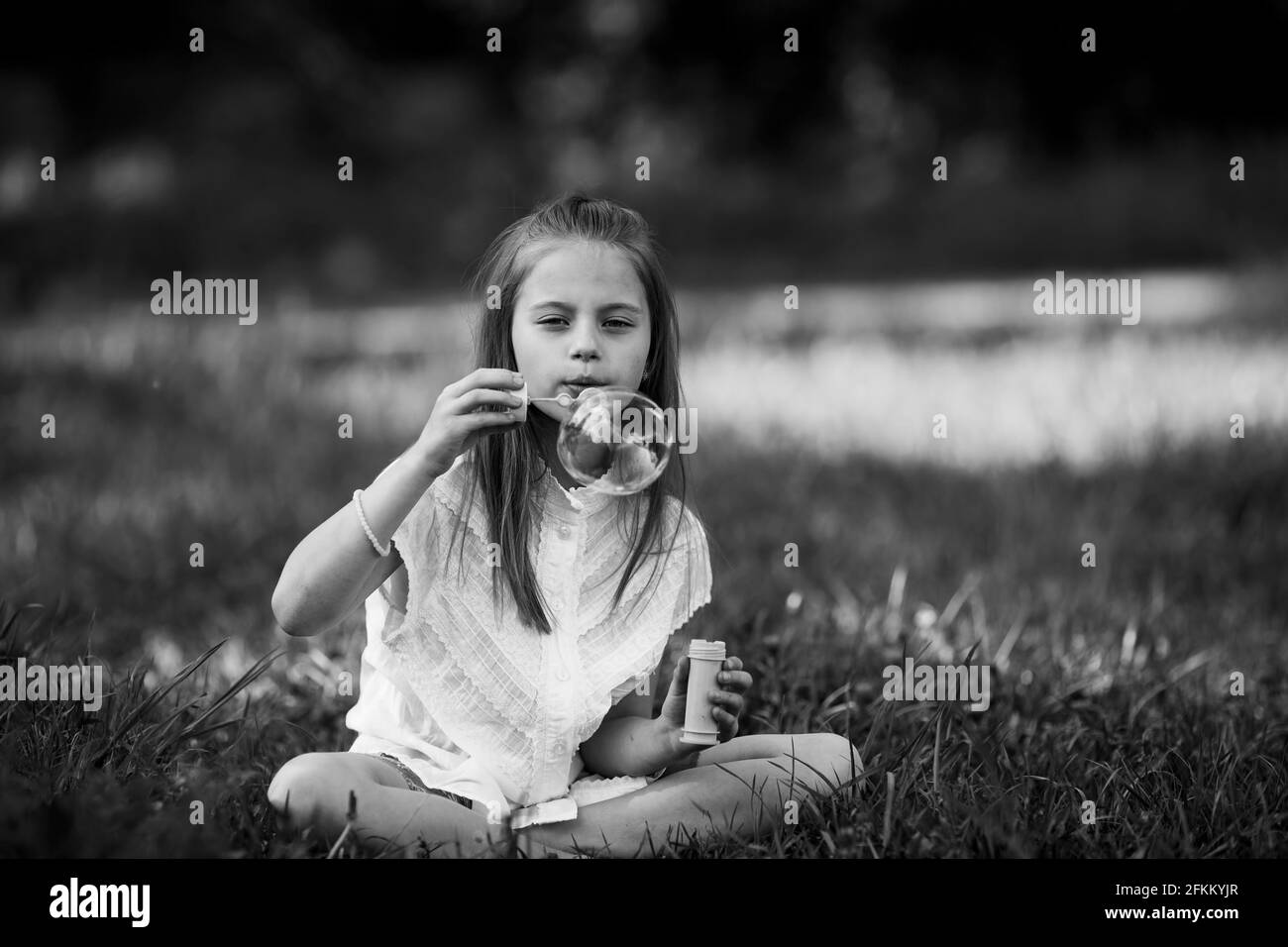 Una bambina gonfia bolle di sapone all'aperto. Foto in bianco e nero. Foto Stock