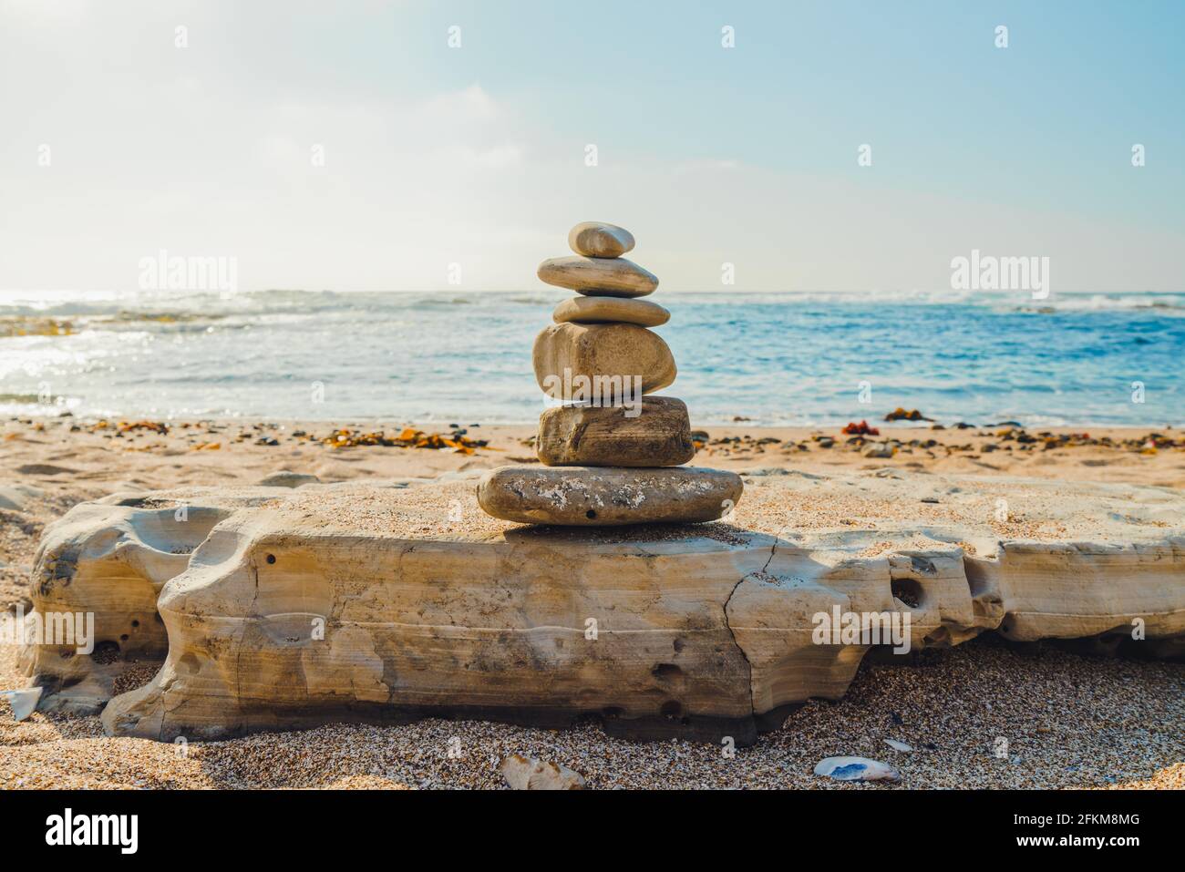 Equilibrio di pietra, piramide di ciottoli sulla spiaggia. Onde di mare dai colori turchesi e cielo blu chiaro sullo sfondo Foto Stock