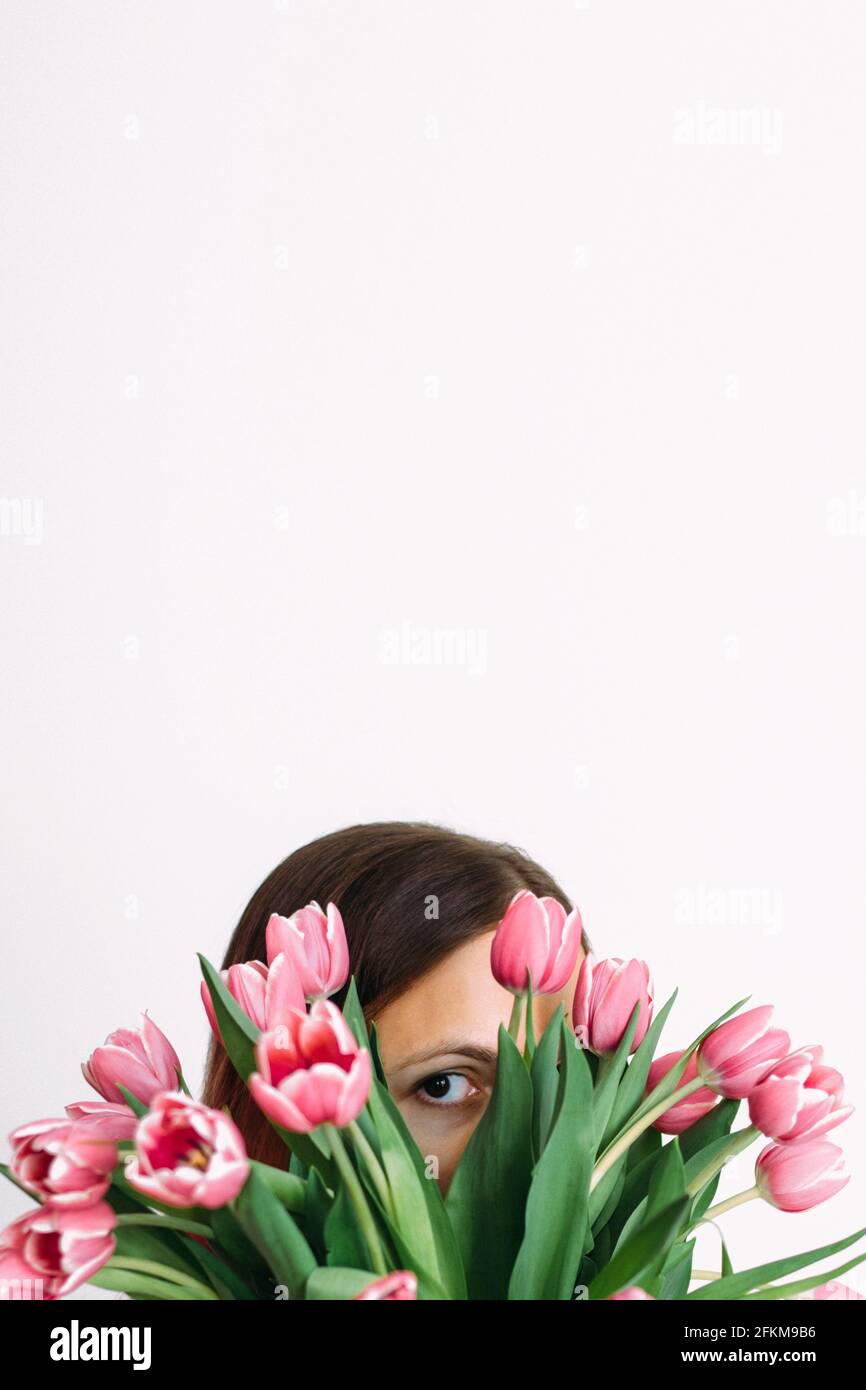Primo piano di una donna che si nasconde dietro i tulipani contro la parete bianca Foto Stock