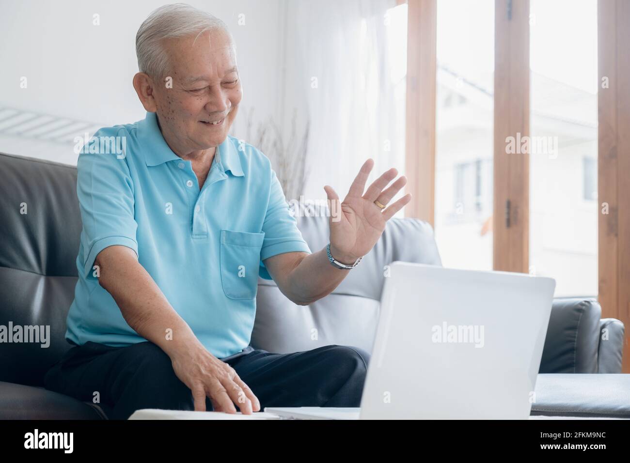 Uomo anziano che fa videochiamata e che sventola sullo schermo. Foto Stock