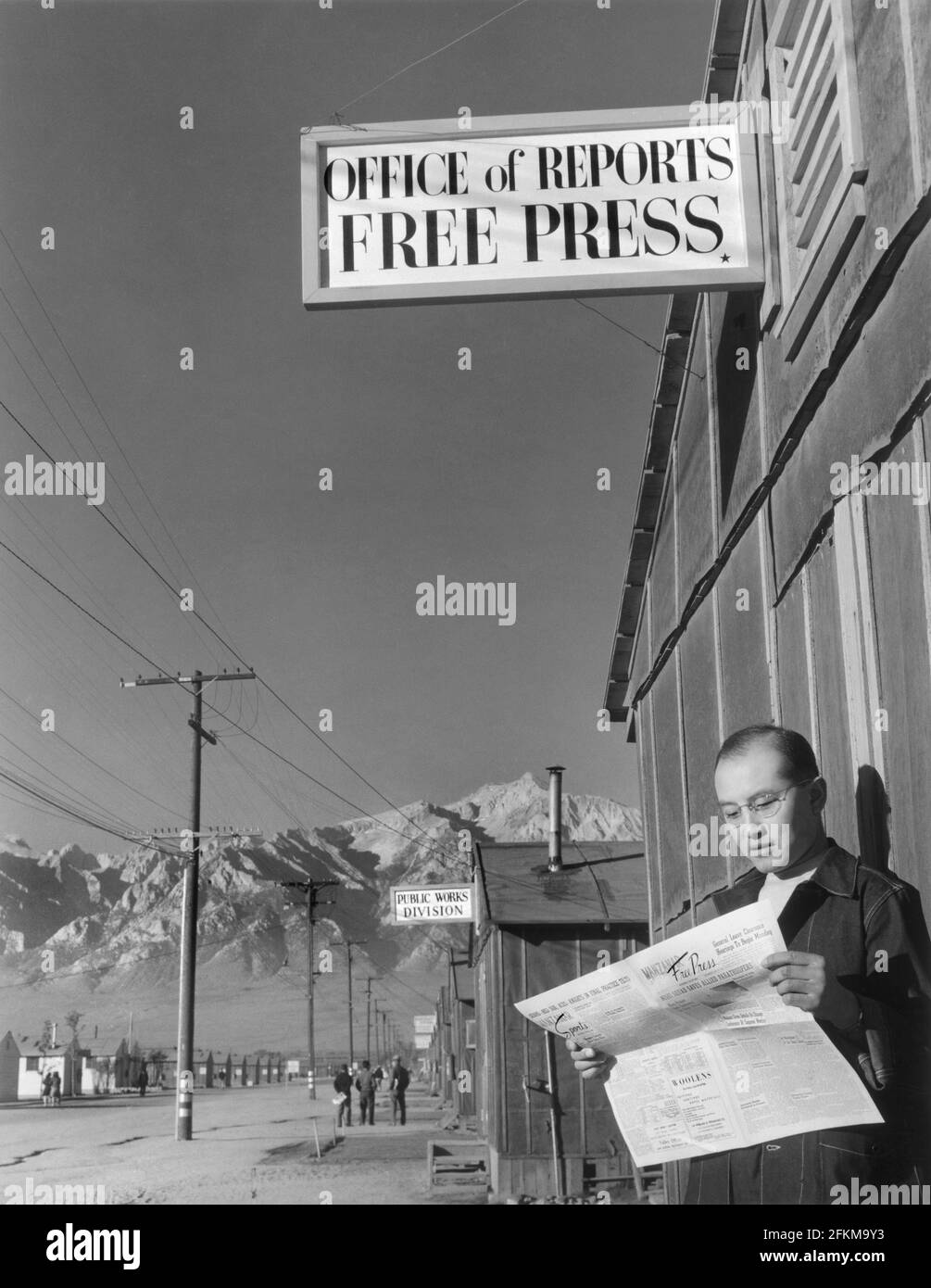 Redattore Roy Takeno Reading Copy of Manzanar Free Press di fronte all'Ufficio del giornale, Centro di Relocation Manzanar, California, USA, Ansel Adams, Manzanar War Relocation Center Collection, 1943 Foto Stock