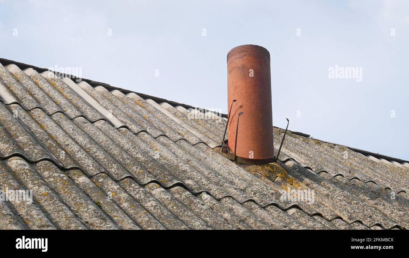 Camino sotto forma di tubo sul vecchio tetto di ardesia del fienile, parzialmente coperto di lichene giallo, contro il cielo Foto Stock