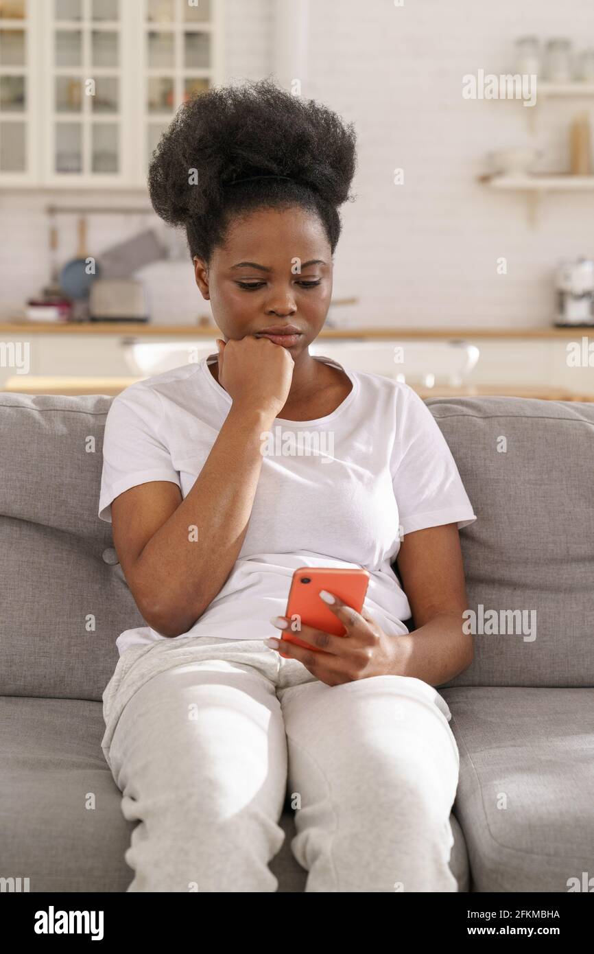 Serio messaggio di lettura femminile nero focalizzato sullo smartphone. La ragazza pensiva ottiene le notizie difettose nell'applicazione del telefono delle cellule Foto Stock