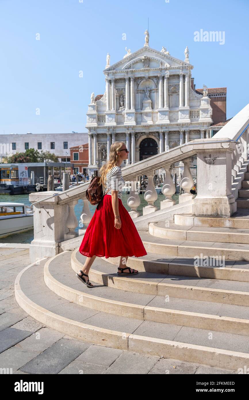 Giovane donna con gonna rossa attraversa un ponte sul Canal Grande, Chiesa di Santa Maria di Nazareth, Ponte degli Scalzi, Venezia, Veneto, Italia Foto Stock