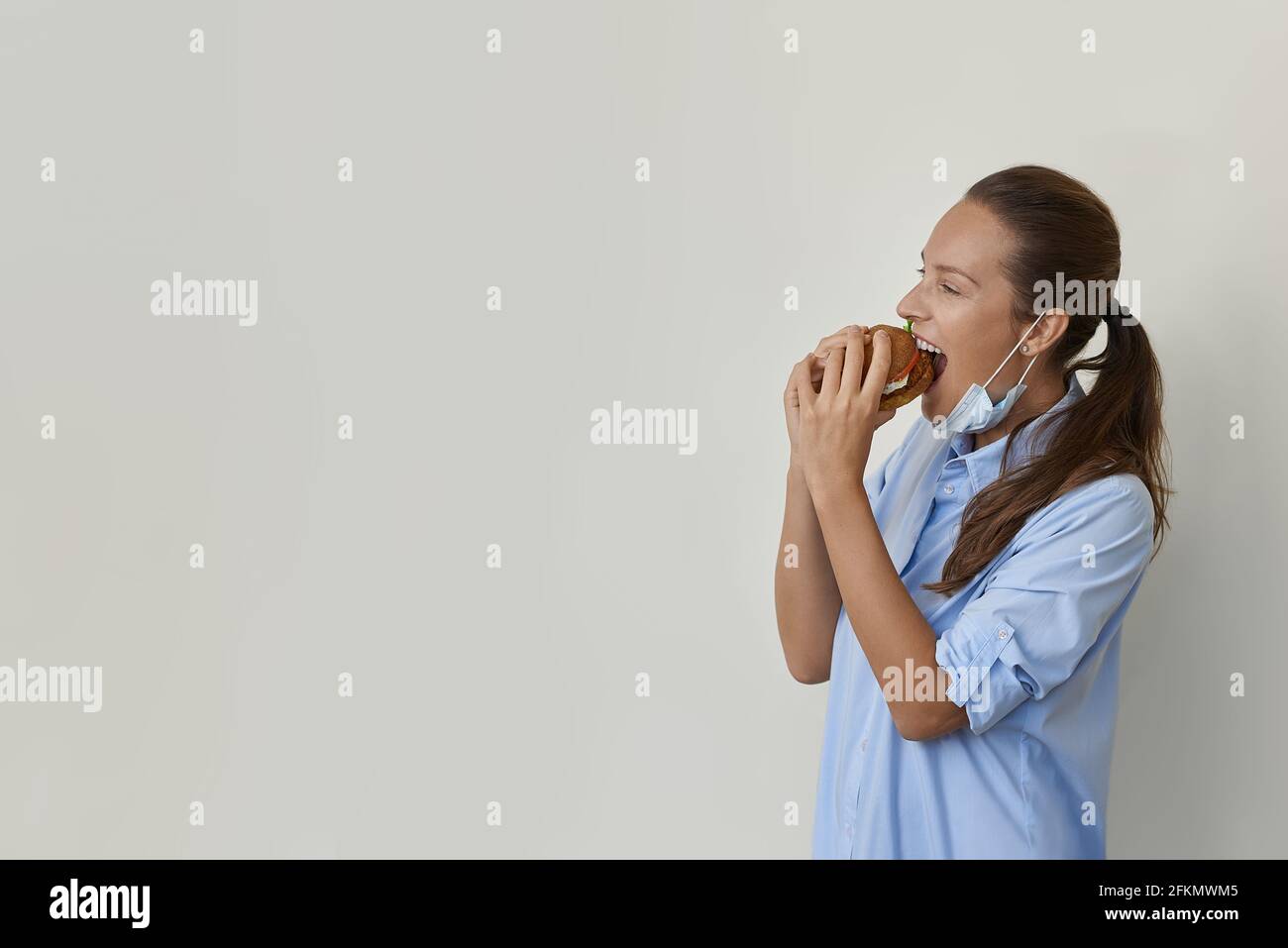 Bella donna in maschera mangiare un hamburger vegan vista laterale Foto Stock