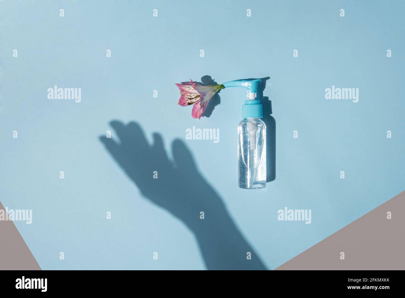 Dispenser con gel trasparente e fiore su sfondo azzurro. Silhouette ombra di una mano femminile. Foto Stock