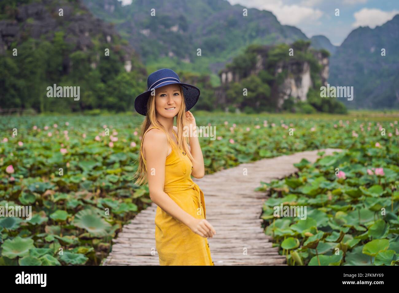 Giovane donna in abito giallo sul sentiero tra il lago di loto. MUA Cave, Ninh Binh, Vietnam. Il Vietnam riapre dopo la quarantena Coronovirus COVID 19 Foto Stock