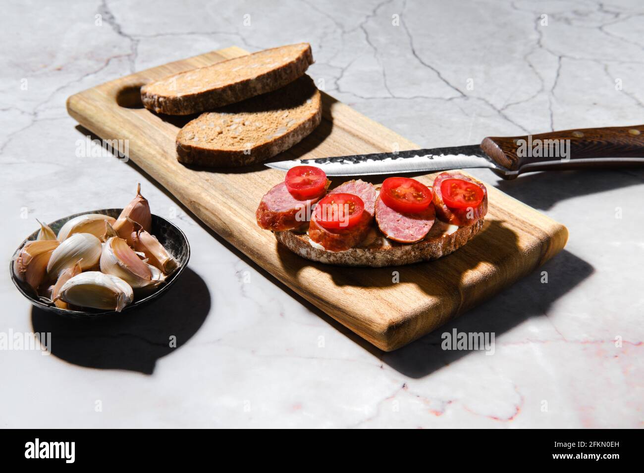 Sandwich con anelli di salsiccia di maiale affumicata su tagliere di legno su tavolo da cucina Foto Stock