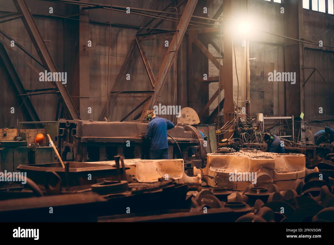 Il lavoratore in officina lavora una grande parte di ghisa dopo la fusione in un impianto di fonderia metallurgica. Foto Stock