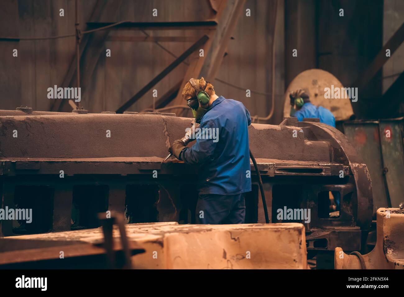 Il lavoratore in officina lavora una grande parte di ghisa dopo la fusione in un impianto di fonderia metallurgica. Foto Stock