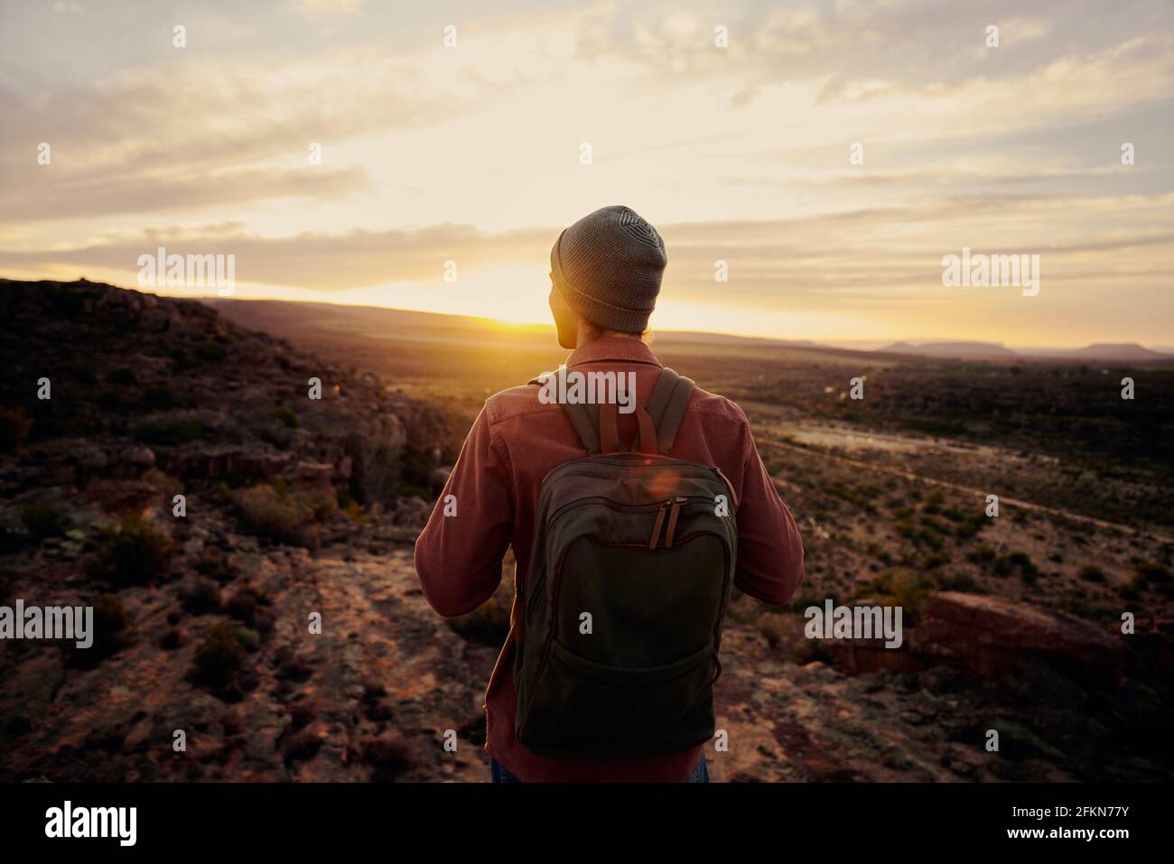Vista posteriore del giovane escursionista maschile in piedi sul bordo di scogliera e godendo l'alba guardando la valle e. montagne Foto Stock