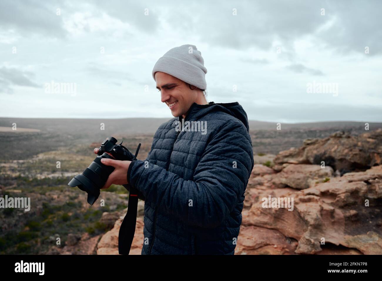 Fotografo di viaggio maschile che controlla le foto sulla fotocamera dopo aver girato in piedi sulla montagnetta Foto Stock