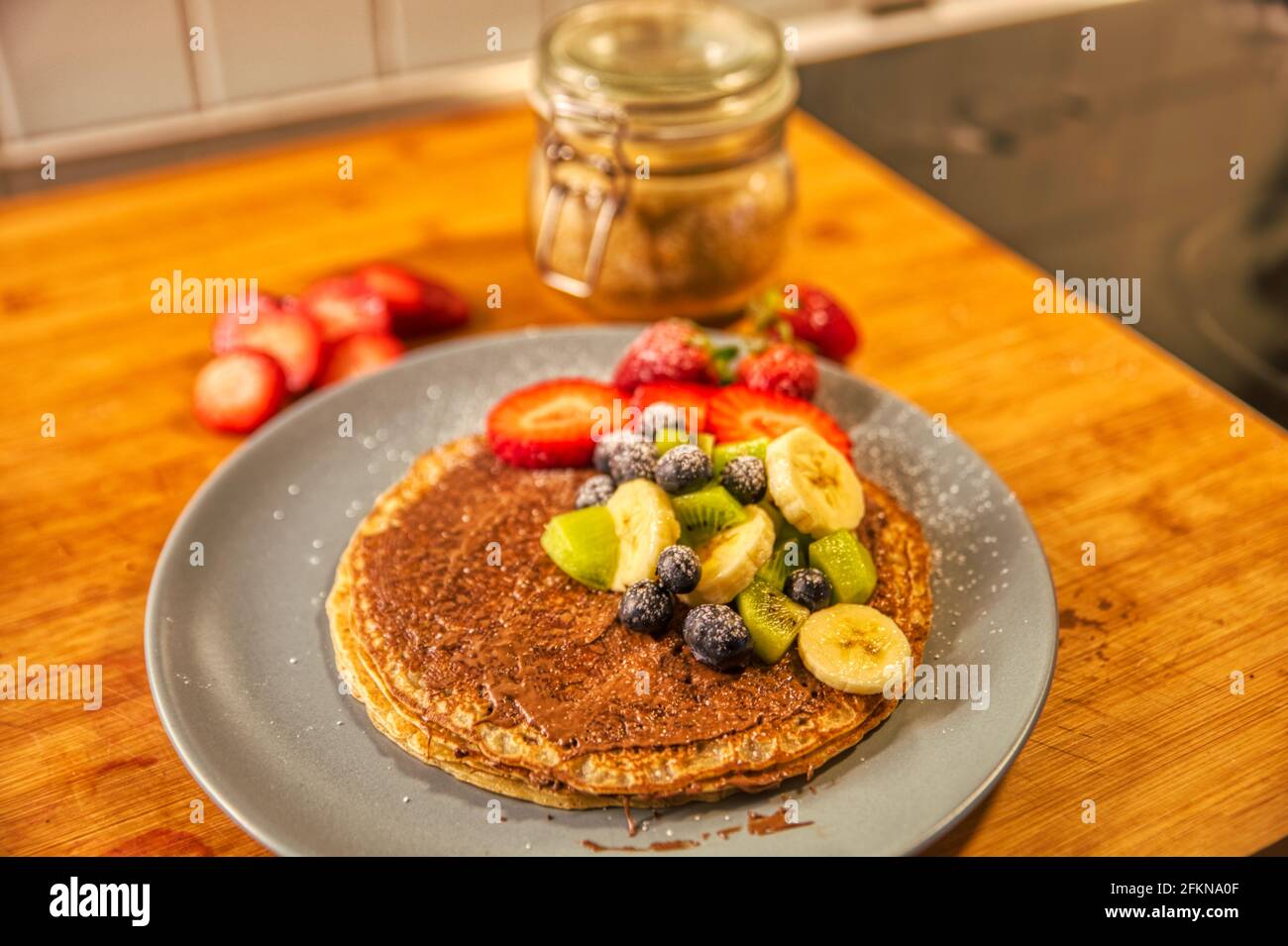 Nocciole di cioccolato rotonde spalmabili crespate o frittelle dolci alla crema di nutella condito con frutta fresca su una tavola rustica di legno e. una spruzzata di zucchero a velo Foto Stock