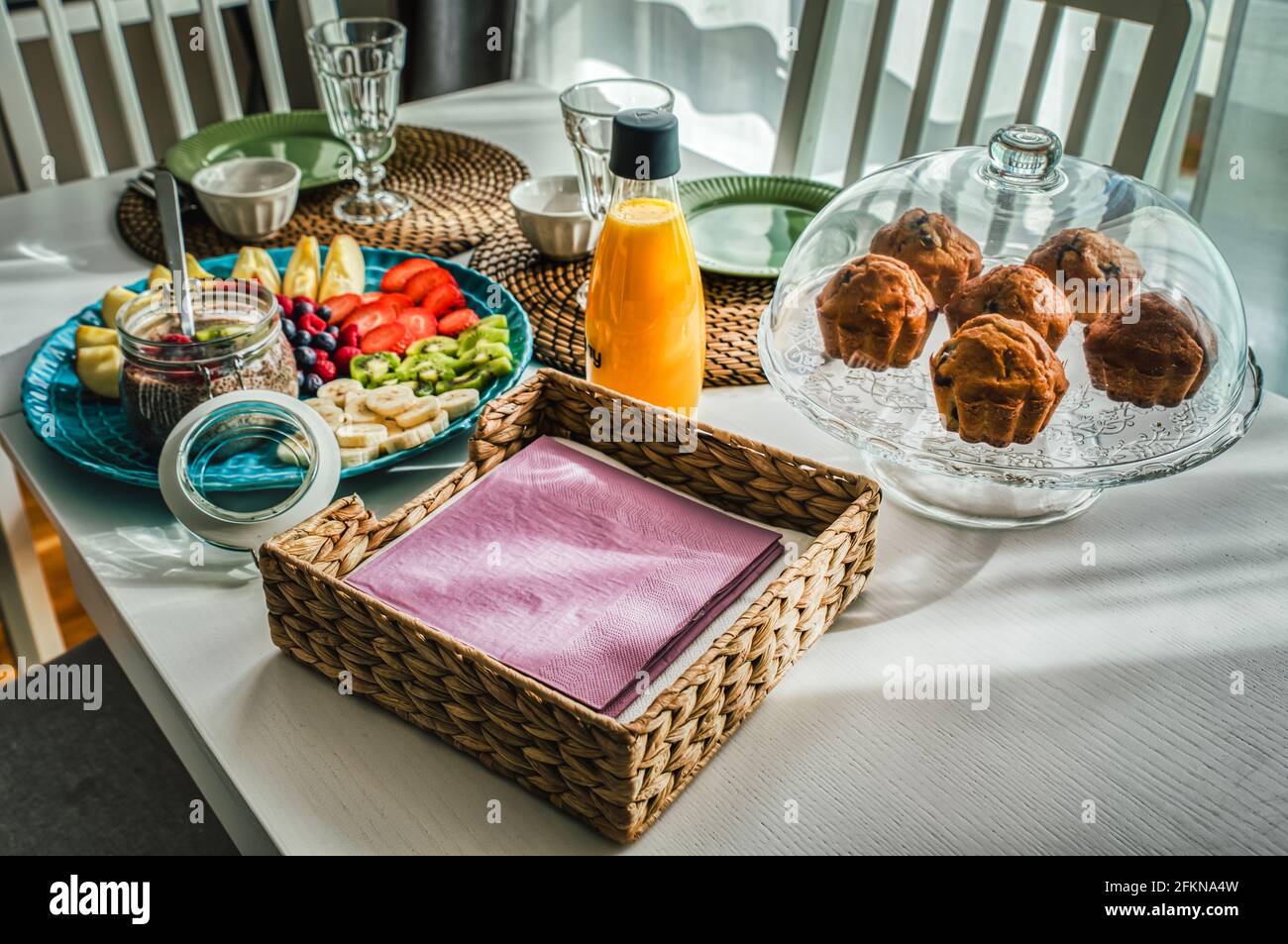 Colazione continentale mattutina con muffin, frutta di stagione come mele, fragole e budino di chia su tavolo di legno bianco con stuoia di paglia rustica Foto Stock