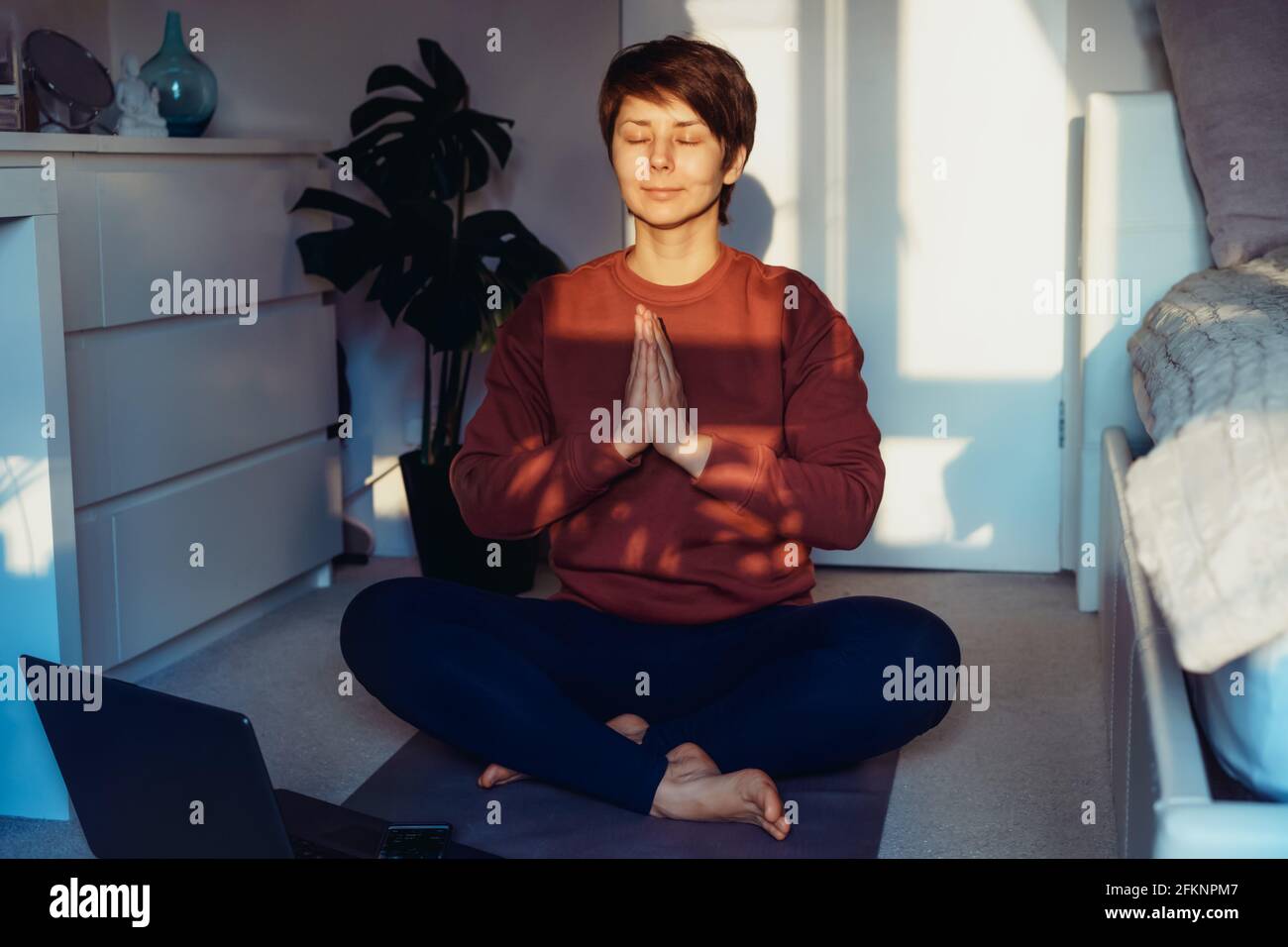 Una donna seduta su un tappetino mentre facendo yoga posizionare Namaste in camera da letto. Relax pratica yoga online a casa. Stile di vita sano. Allenamento online a casa Foto Stock