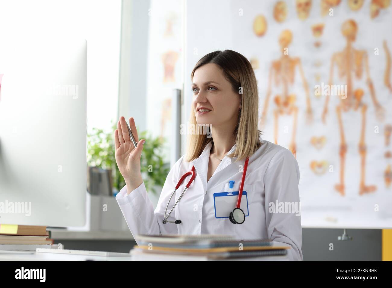 Donna dottore siede al tavolo e agita sullo schermo del computer Foto Stock