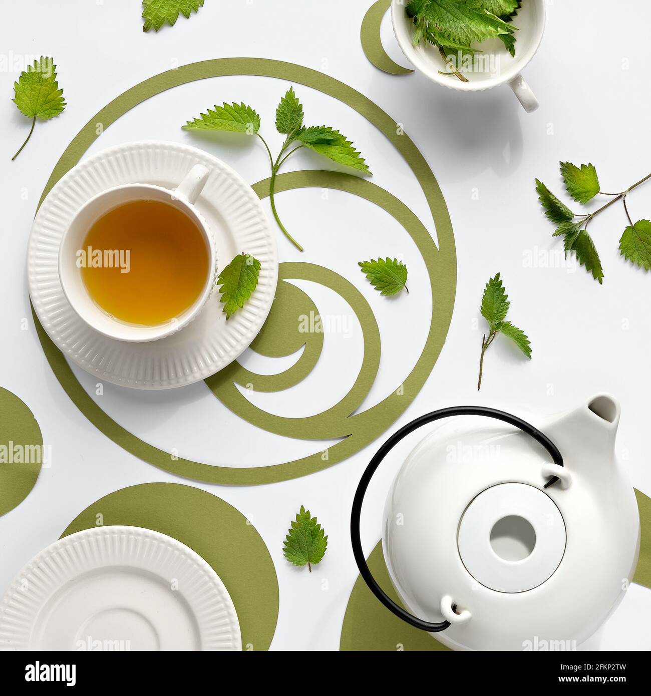 Tazza di tè di ortica, foglie di erbe di ortica pungente. Posa piatta ornata, carta verde Fibonacci sequenza cerchi su sfondo bianco spento. Medicina alternativa Foto Stock