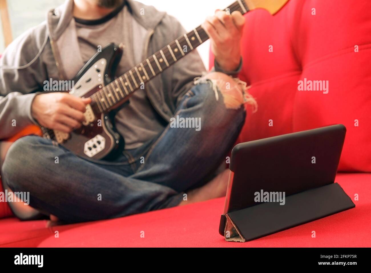 Giovane uomo casual in jeans strappati, suonando sunburst offset chitarra elettrica. Giovane musicista che prende online strumento musicale corso di lezione su wireless i Foto Stock