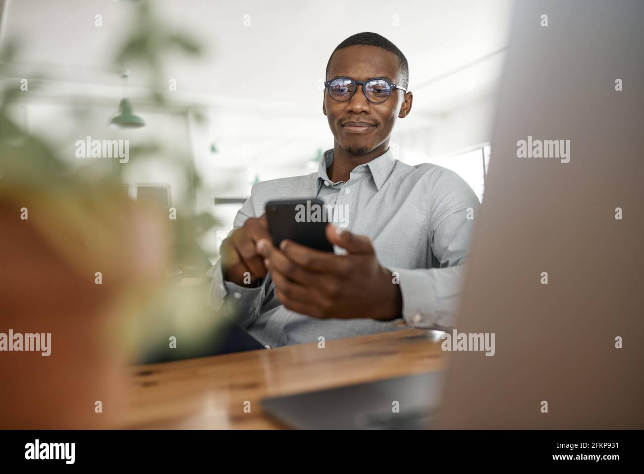 Giovane uomo d'affari africano che SMS sul suo telefono al lavoro Foto Stock