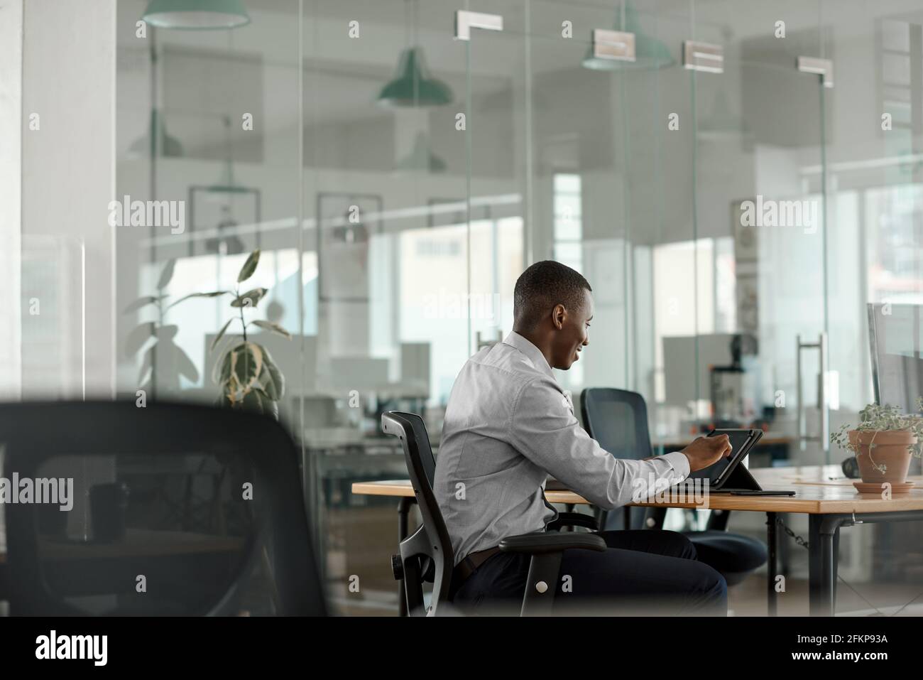Sorridente uomo d'affari africano utilizzando un tablet a un tavolo da ufficio Foto Stock