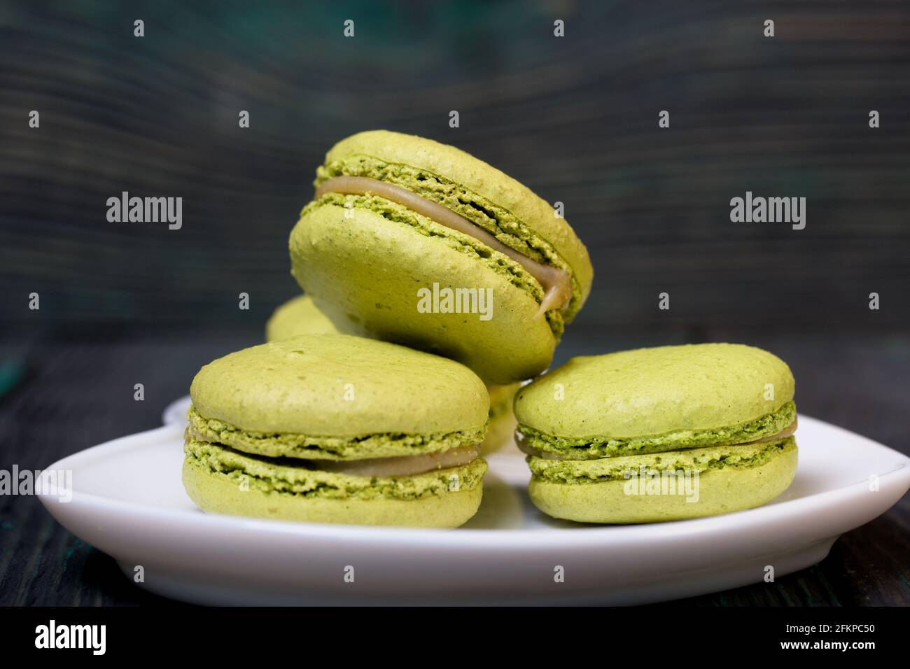 Macaron verde chiaro giacciono su un piatto. Su assi di pino con una texture legnosa croccante. Foto Stock