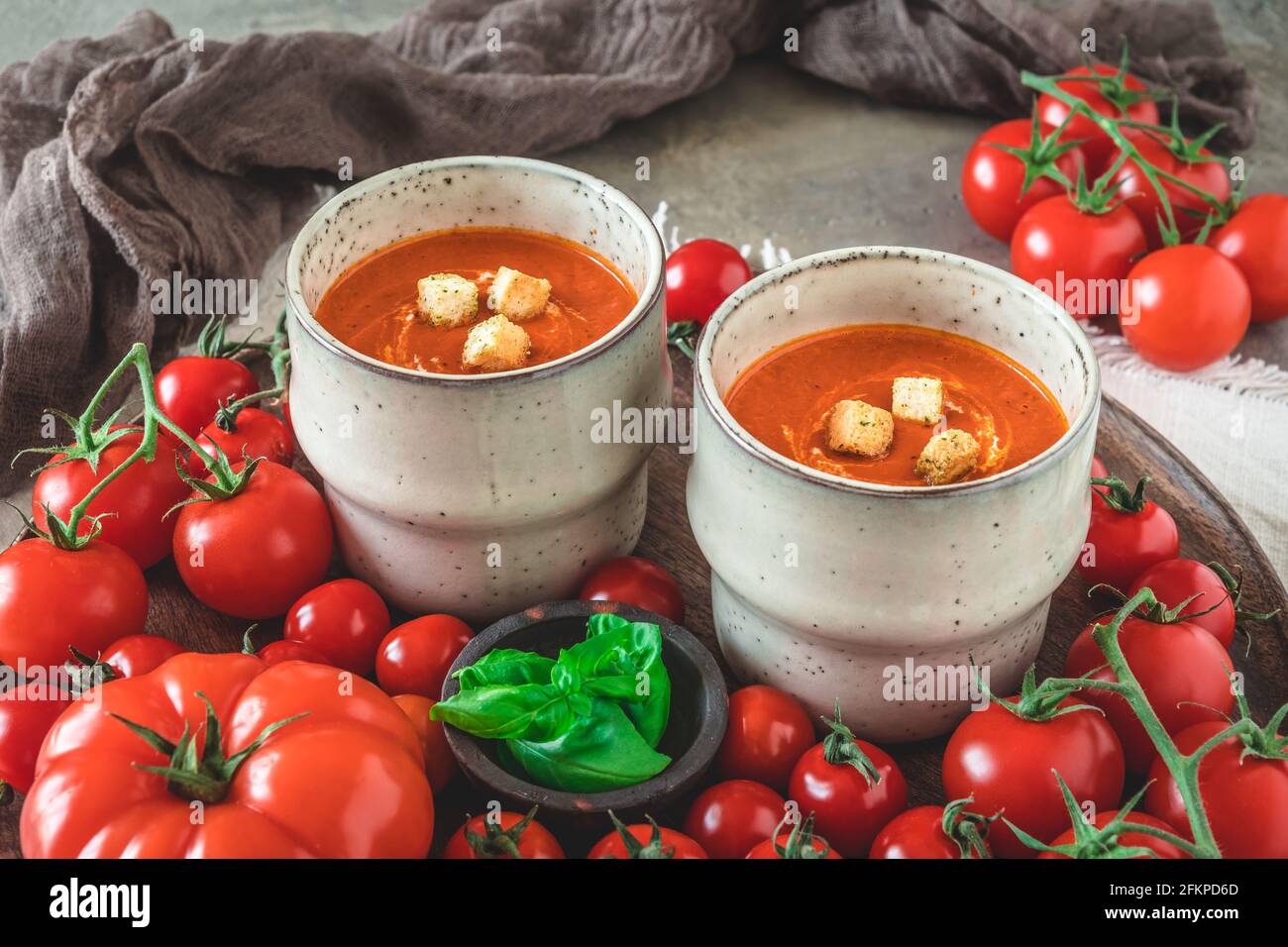 Due tazze riempite con zuppa di pomodoro fresca fatta in casa su un vassoio di legno con una varietà di pomodori maturi Foto Stock