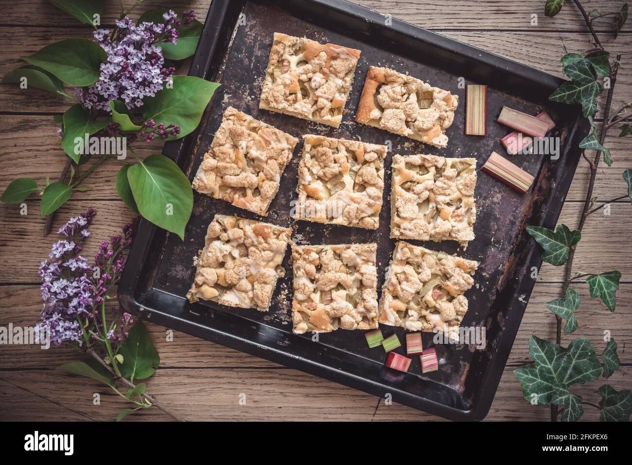 Vassoio da forno con pezzi di torta briciola su fondo di legno, decorato con fiori di lilla, vista dall'alto Foto Stock