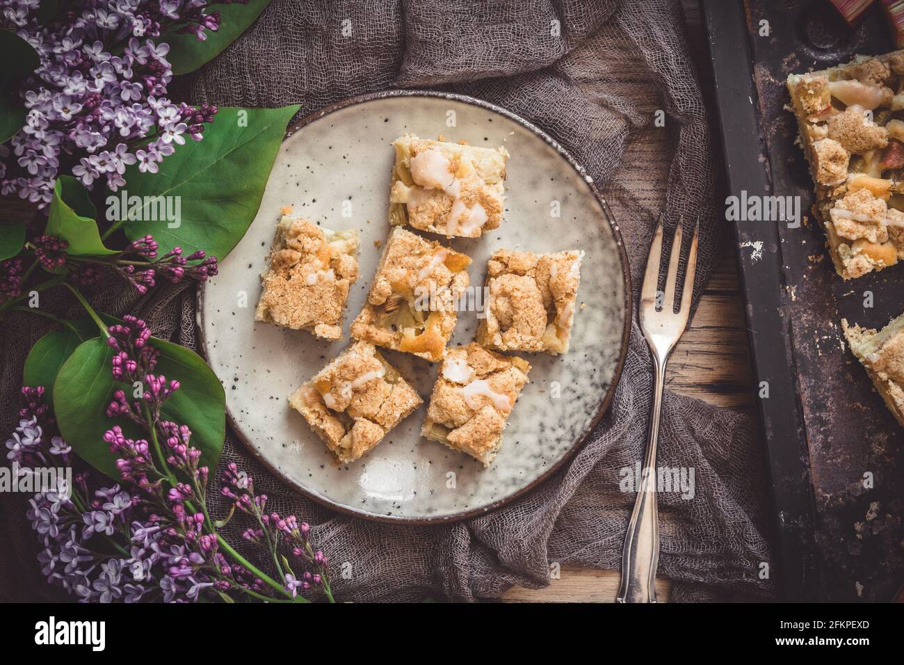 Pezzi di torta sbriciola di rabarbaro su un piatto su fondo di legno, decorato con fiori di lilla, vista dall'alto Foto Stock