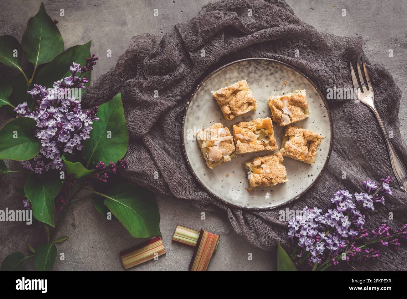 Pezzi di torta sbriciola di rabarbaro su un piatto su sfondo grigio, decorato con fiori di lilla, vista dall'alto Foto Stock