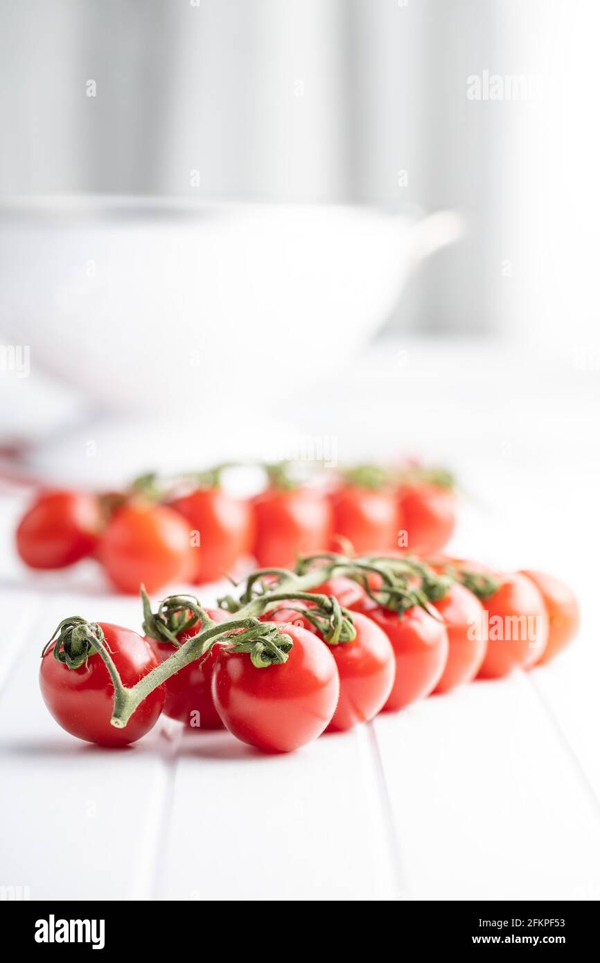 Pomodori ciliegini rossi freschi. Pomodori piccoli sul ramo su tavola bianca. Foto Stock