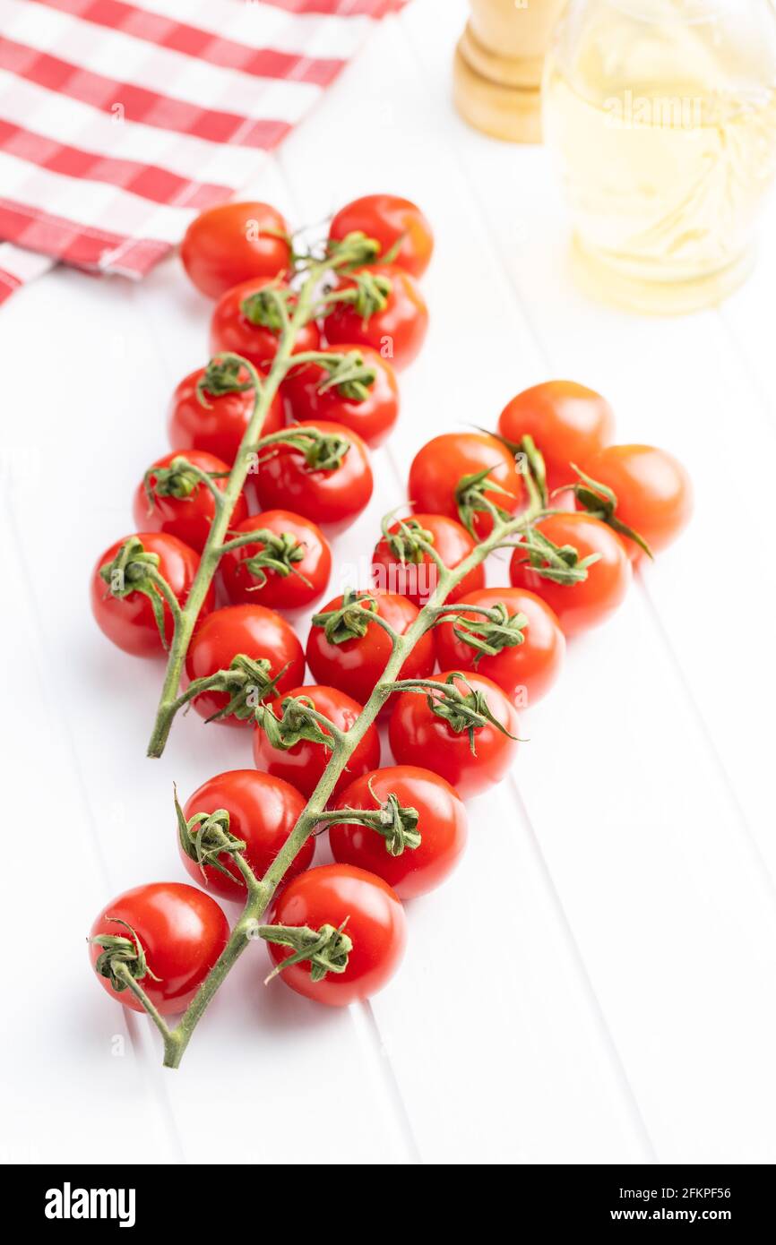 Pomodori ciliegini rossi freschi. Pomodori piccoli sul ramo su tavola bianca. Foto Stock