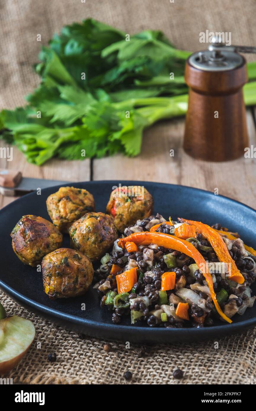 Palle di verdure grigliate con insalata di lenticchie su piatto nero su tavolo di legno, concetto di cibo vegano, foto verticale di stock Foto Stock
