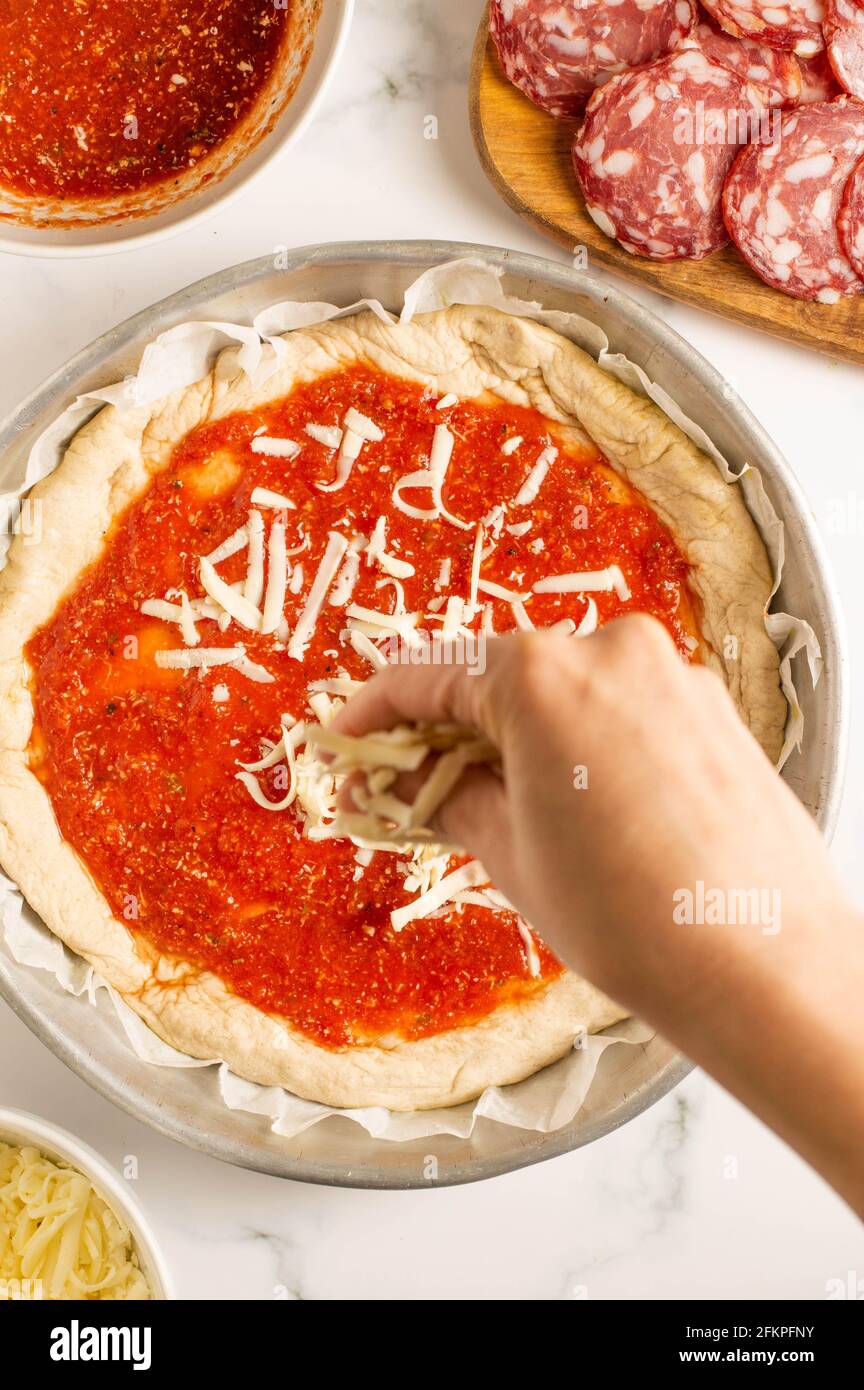 Pizza pepperoni in preparazione: Pasta per pizza in padella con salsa di  pomodoro in cima. Fuoco selettivo sull'impasto e una mano della donna con  alcuni chee della mozzarella Foto stock - Alamy