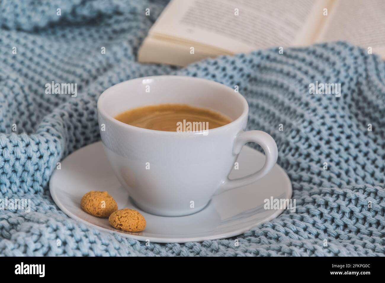 Tazza di caffè su una coperta di lana di maglia blu chiaro. Atmosfera accogliente. Pausa caffè, concetto di soggiorno a casa. Foto Stock