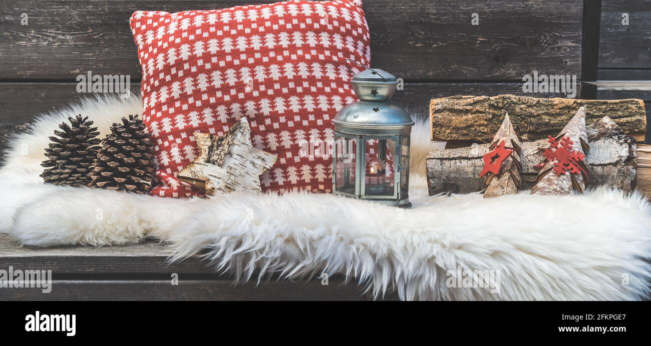 Veranda in legno con pelle di agnello, cuscini natalizi rossi e bianchi, lanterna e tronchi Foto Stock