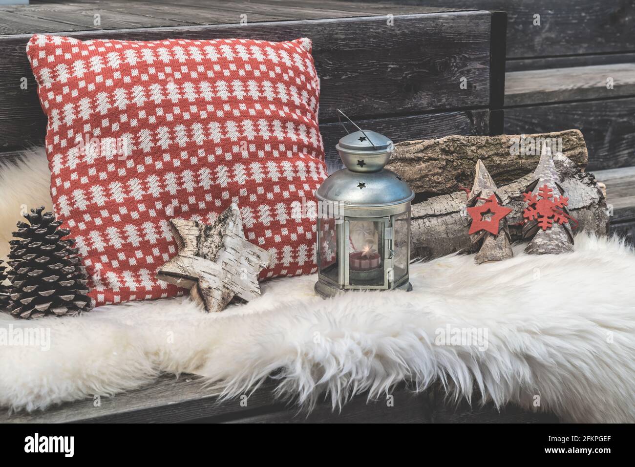 Veranda in legno con pelle di agnello, cuscini natalizi rossi e bianchi, lanterna e legna da ardere Foto Stock