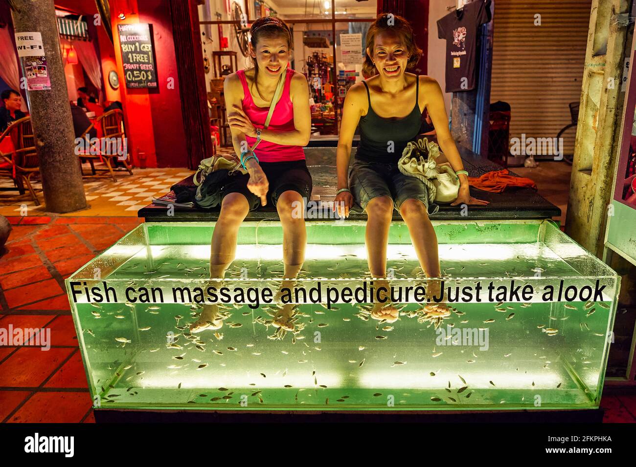 Due donne sorridenti che hanno un pedicure di massaggio di pesce in un centro di massaggio di Siem Reap. Cambogia. Foto Stock