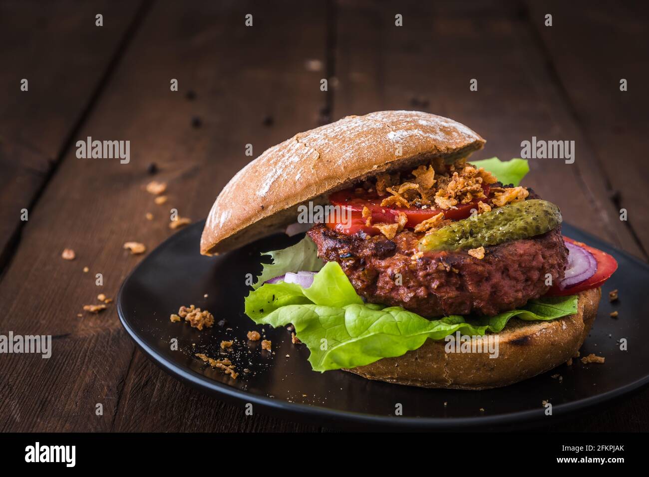Burger con polpettine vegetariano di hamburger, insalata, pomodori e cipolle arrostite su un piatto nero su tavolo di legno, spazio copia Foto Stock