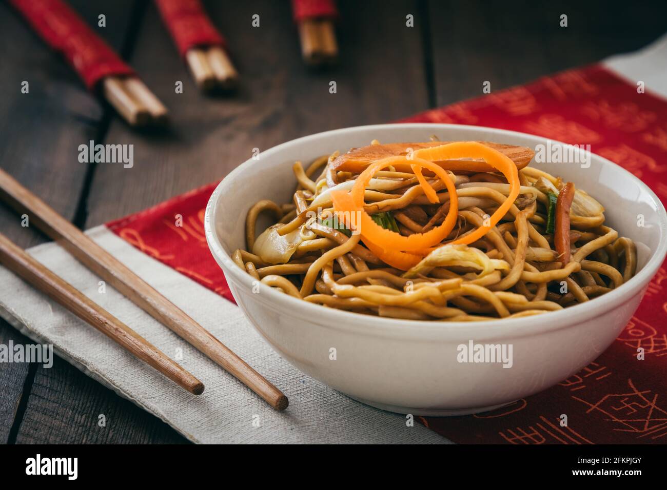 Tagliatelle vegetariane cinesi in una ciotola bianca sul posto cinese tappetino su tavolo di legno Foto Stock