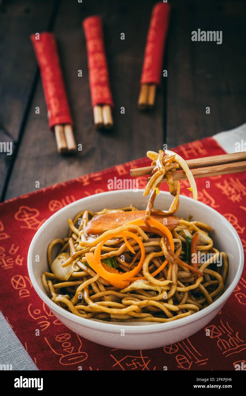 Tagliatelle vegetariane cinesi in una ciotola bianca su tappetino cinese posto su tavolo di legno, foto verticale stock Foto Stock