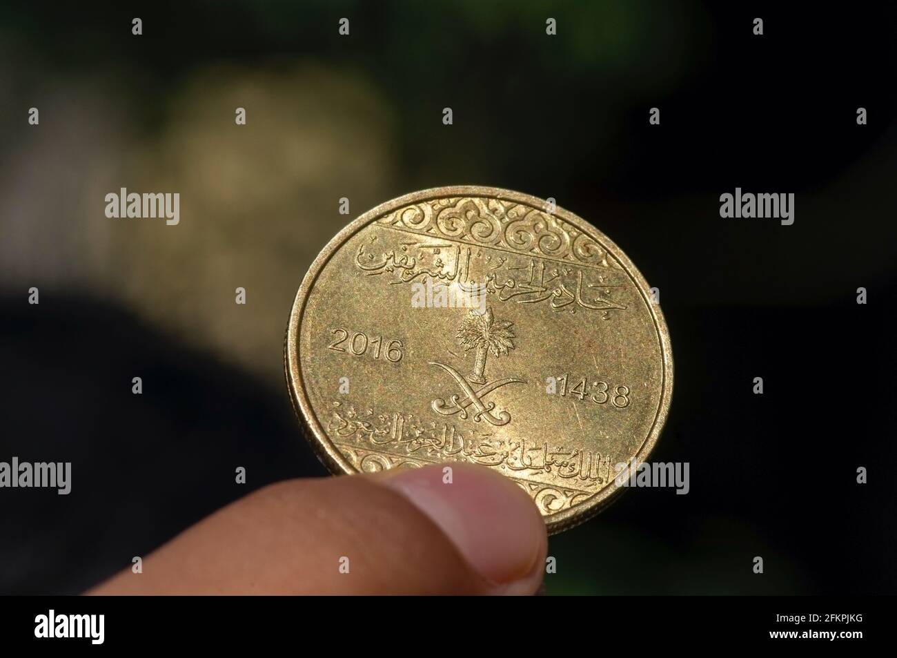 Mano del bambino asiatico che tiene una cinquanta moneta di Riyal di Halalas, soldi dell'Arabia Saudita, fuoco selezionato e sfondo scuro Foto Stock