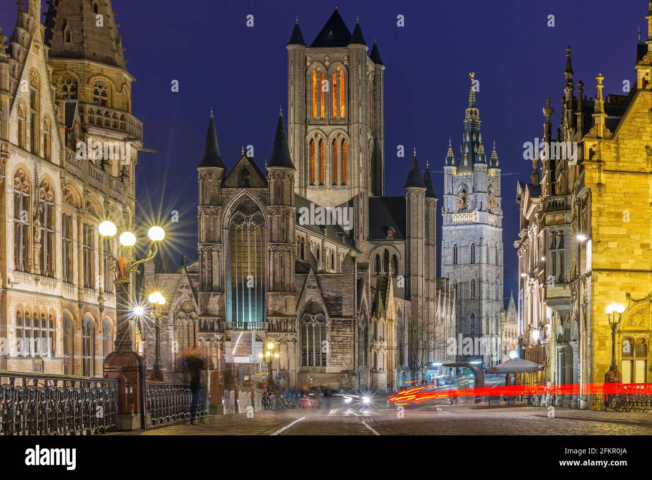 Gand (Gent) centro della città di notte con il movimento offuscato di persone e mezzi di trasporto con la Cattedrale di San Bavo e il campanile, Fiandre, Belgio. Foto Stock