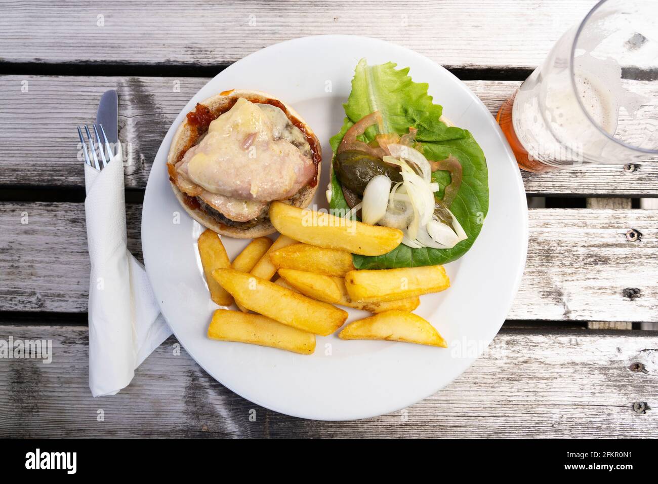 Piatto principale ben presentato di un hamburger e patatine con una pinta di birra su un tavolo di legno all'esterno al pub Bolton Arms in Old Basing, Hampshire, Regno Unito Foto Stock