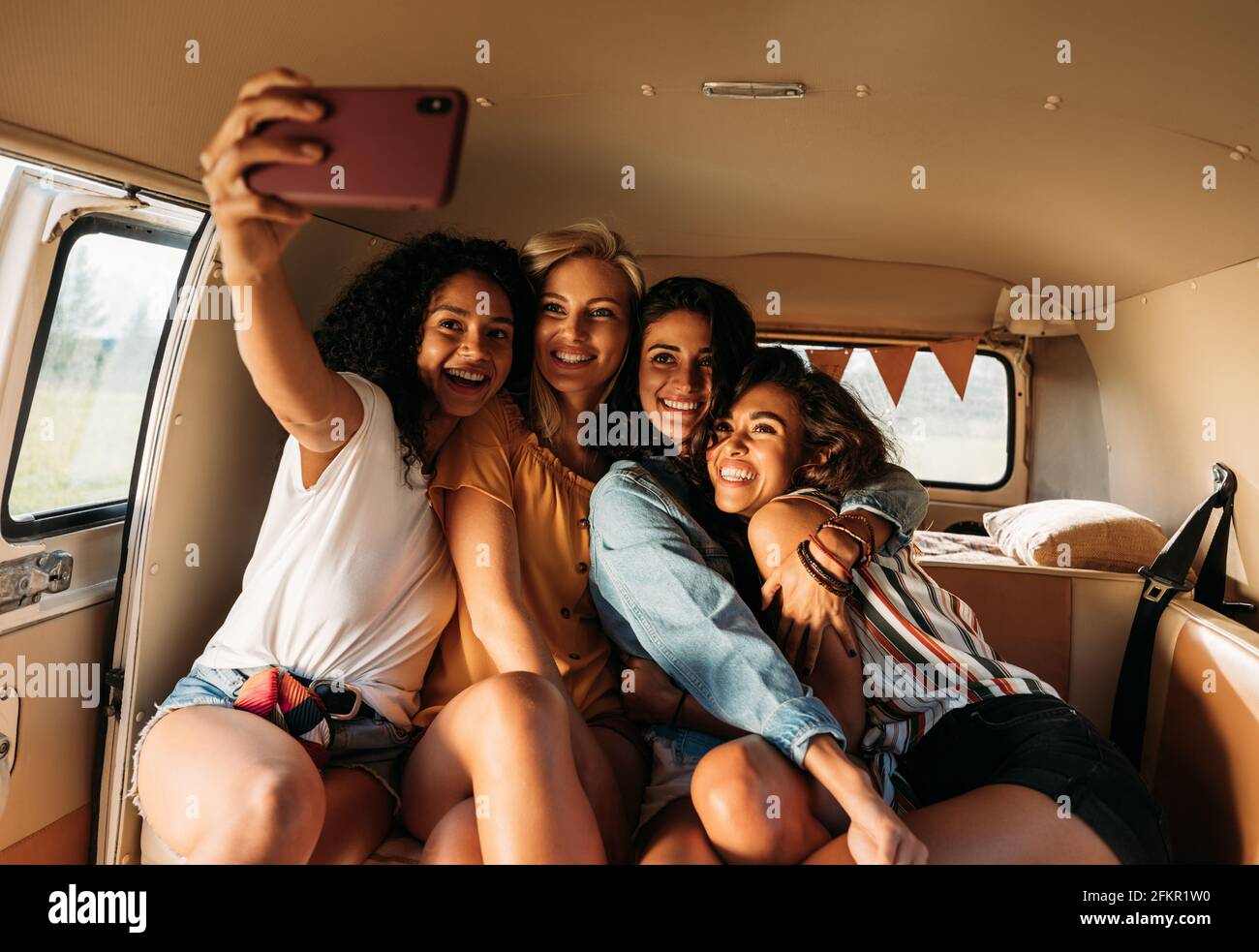 Quattro bellissimi amici che prendono selfie in un furgone durante un viaggio in auto. Donne sorridenti in vacanza. Foto Stock