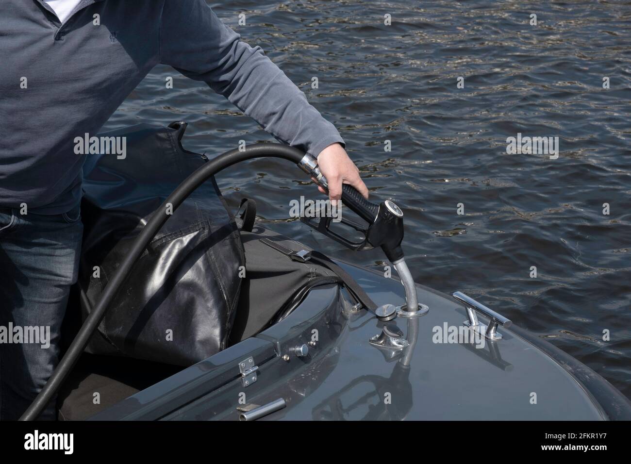 L'uomo ha una pistola a carburante in mano e riempie il serbatoio della sua barca di benzina. Mettere a fuoco il bocchettone di riempimento e il tappo del serbatoio Foto Stock