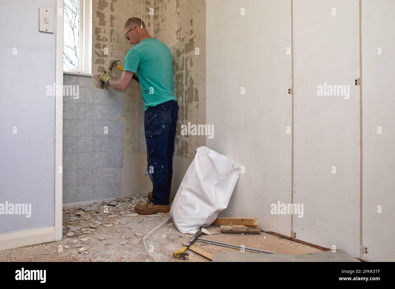 Handyman che lavora alla ristrutturazione della casa rimuovendo le piastrelle di ceramica da un muro. Foto Stock