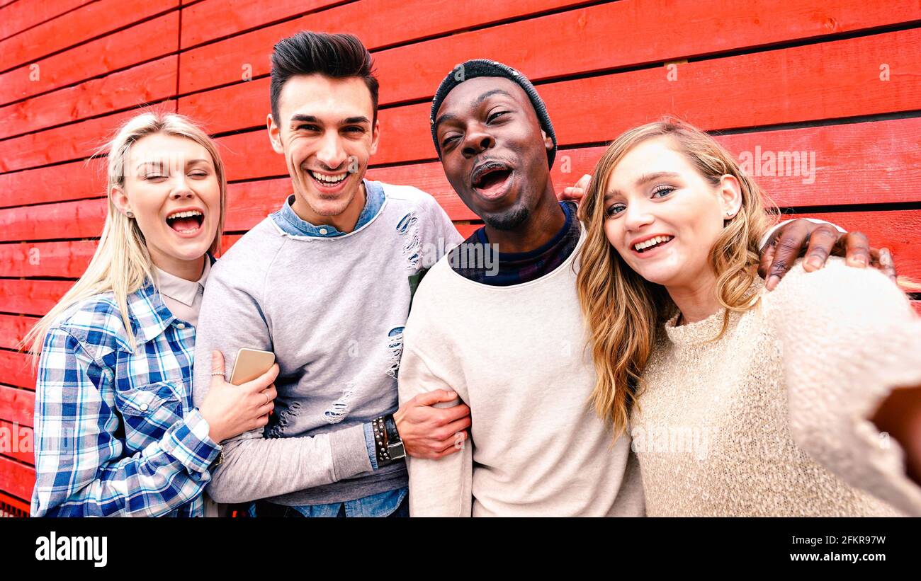 Amici multirazziali felici che prendono selfie di gruppo a sfondo di legno rosso - persone milleniali che condividono storie divertenti sulla comunità dei social media Foto Stock